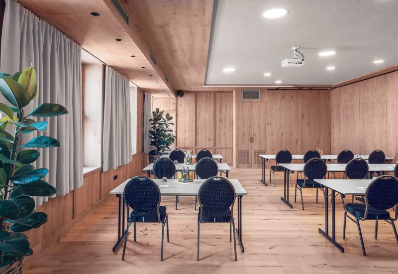 Ein Konferenzraum mit weißem Tische, schwarze Stühle mit gepunktetem Muster, natürlichem Holzinterieur und großen Fenstern mit weißen Vorhängen, die vom Licht durchflutet werden, sowie einigen Pflanzen als Dekoration.