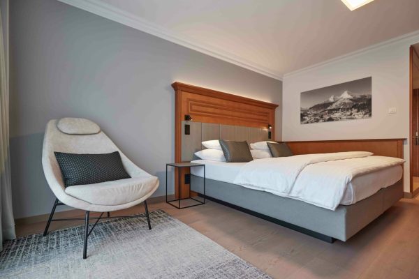 Ein Hotelzimmer mit einem großen, gemachten Bett mit weißen Bettwäsche und mehreren Kissen, einer modernen Stuhl mit Kissen, einer kleinen Nachttisch, einer Wand mit einem schwarzen und weißen Berglandschaftsfoto und stilvoller Raumdeko.