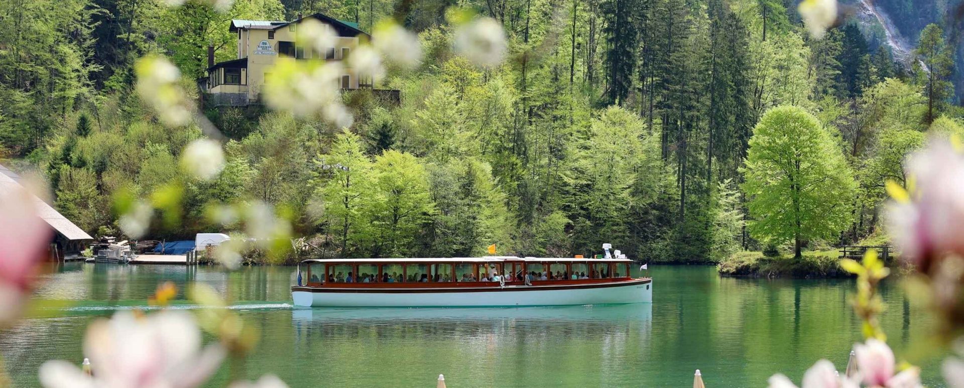 Ein Boot mit Passagieren fährt über einen ruhigen, grünen See, umgeben von einer bewaldeten, hügeligen Landschaft.