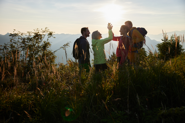 Fünf Wanderer hoch oben in den Bergen, die sich bei Sonnenuntergang treffen und sich gegenseitig high-five geben, um ihre Gemeinschaft zu feiern.