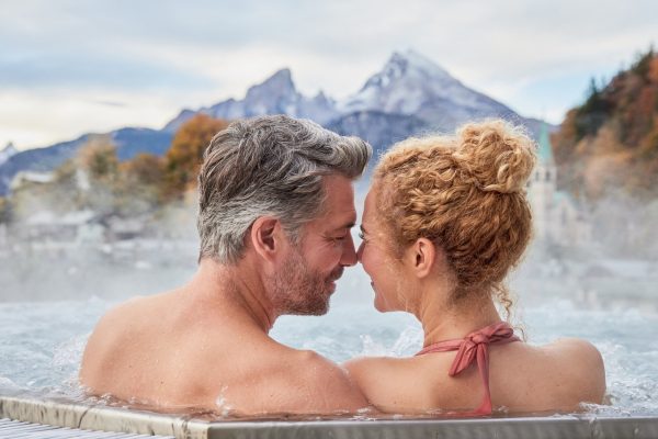 Ein Mann und eine Frau im Whirlpool mit Stirn an Stirn - im Hintergrund ein Berg in bewölkter Stimmung
