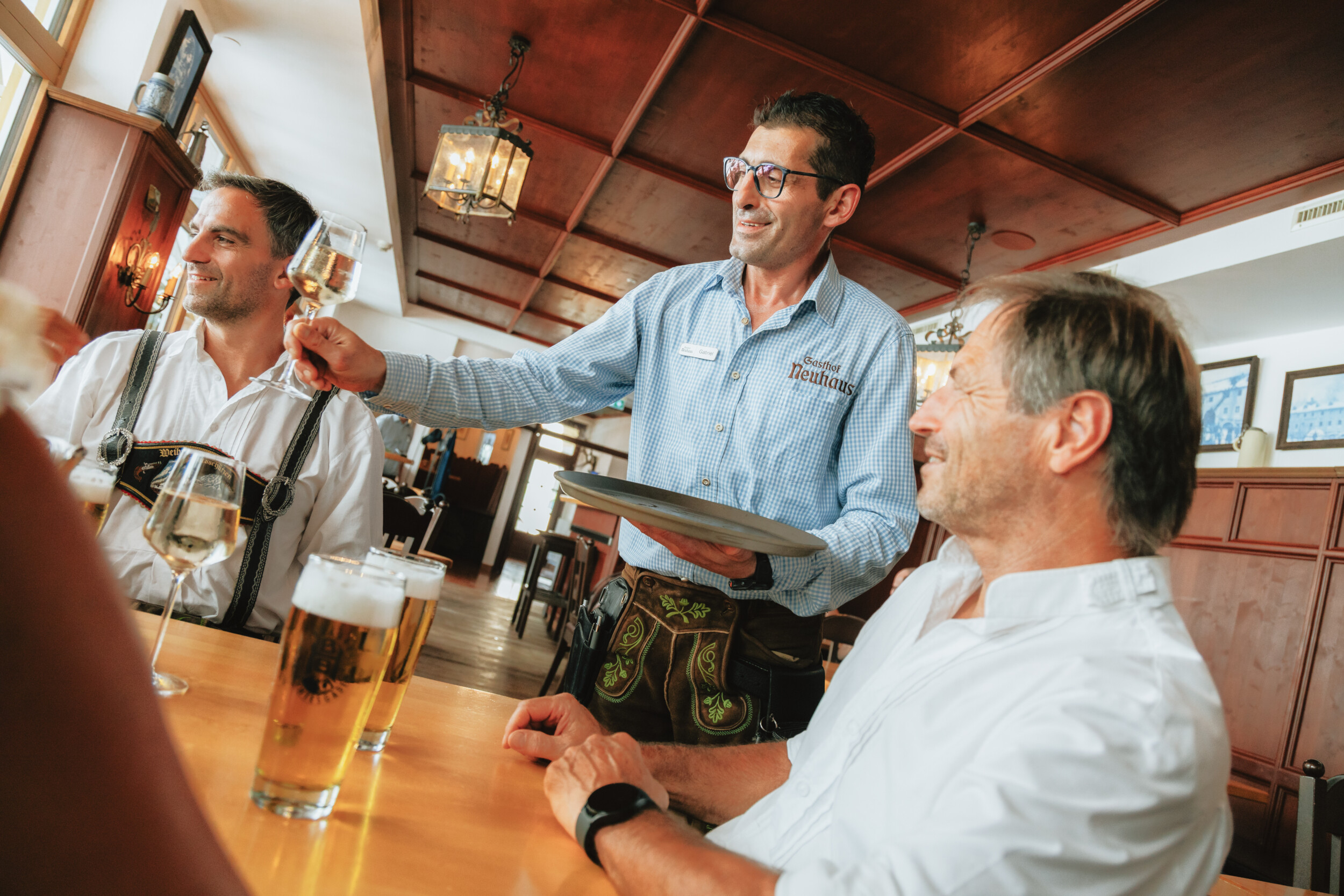 Traditionelle Berchtesgadener Gasthausstube im Gasthof Neuhaus mit Bedienung und Gästen in Tracht bei Wein und Bier.