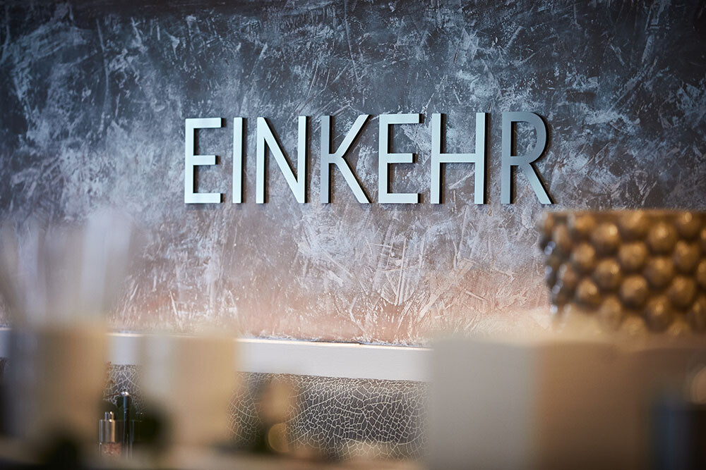 Der Schriftzug "EINKER" an einer rauen, grauen Wand in einem Innenraum, mit unscharfen Gegenständen im Vordergrund.