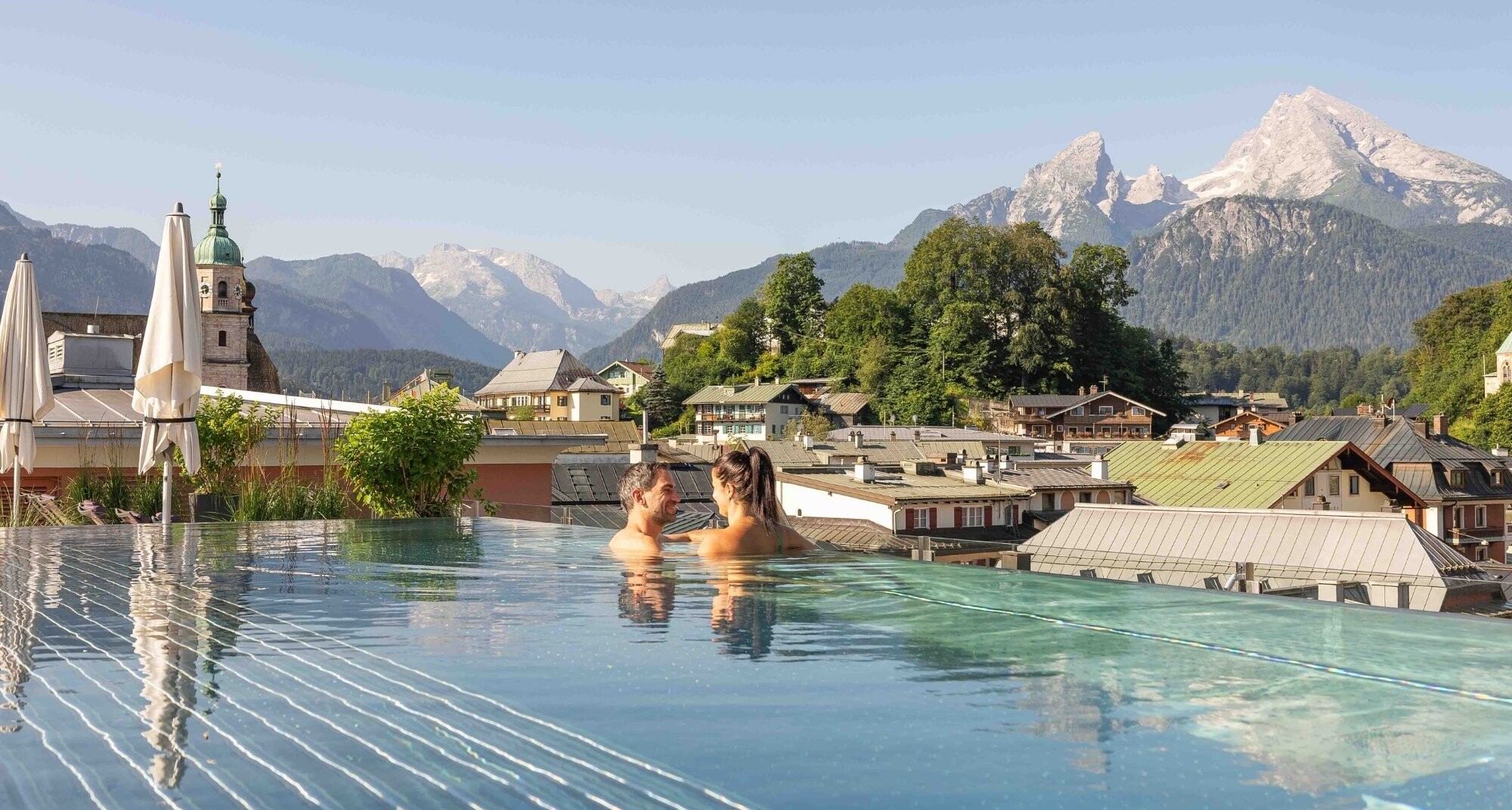 Infinity Pool auf der Dachterrasse des Hotel EDELWEISS Berchtesgaden mit Blick auf die Alpen und den Watzmann, Paar entspannt im warmen Wasser