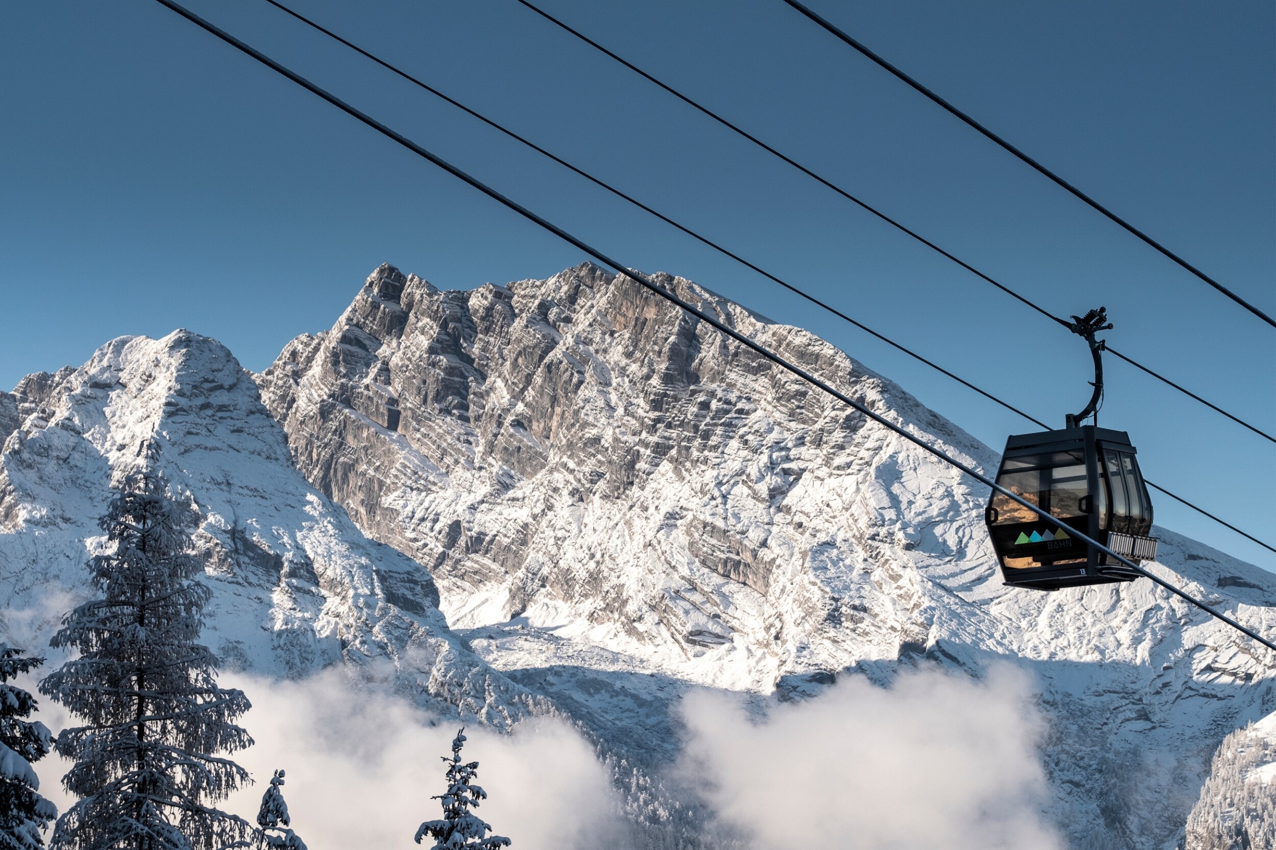 Eine Seilbahn vor verschneiten Berggipfeln und einer klaren blauen Himmel.