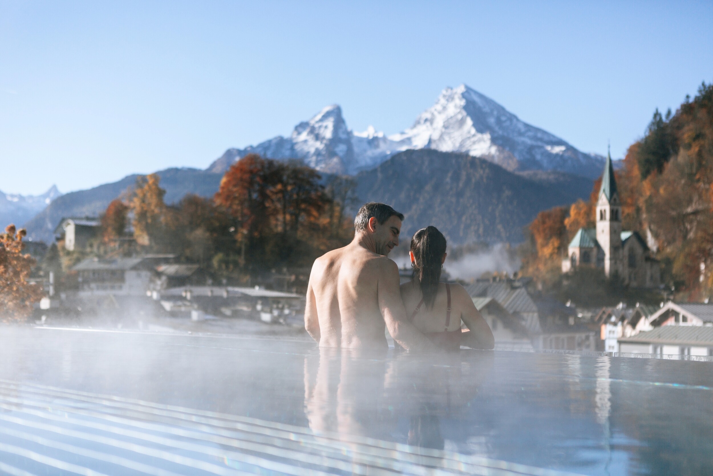Ein Paar genießt die Ruhe im Rooftop Infinity Whirlpool über den Dächern Berchtesgadens - Winterwellness pur.