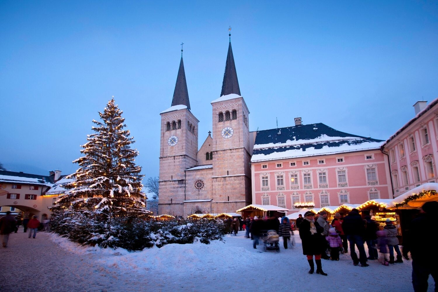 Berchtesgadener Advent mit festlich beleuchtetem Weihnachtsbaum, traditionellen Marktständen und verschneitem Schlossplatz vor der Stiftskirche.