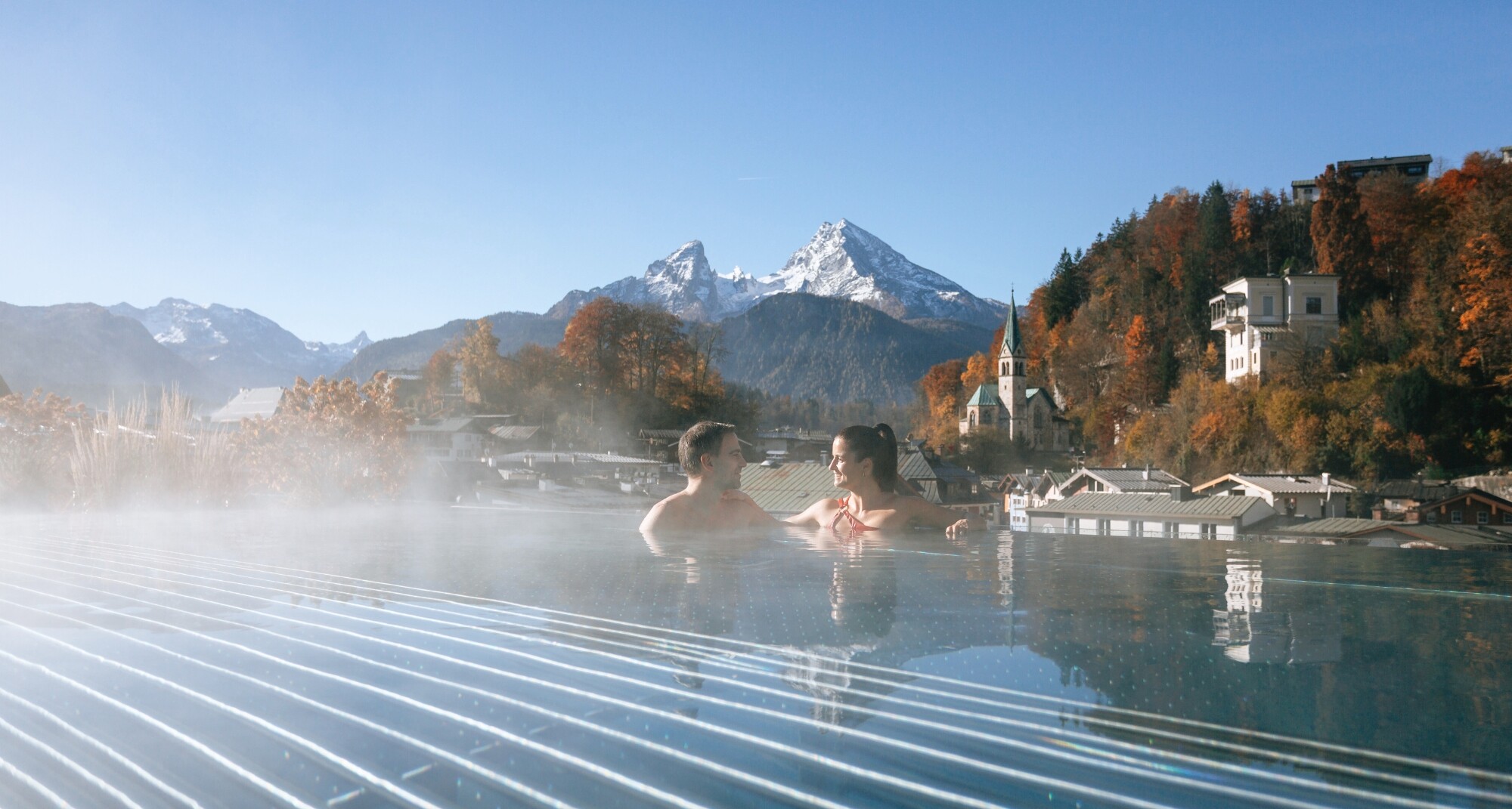 Couple relaxing in an outdoor infinity jacuzzi overlooking the mountains during sunrise or sunset