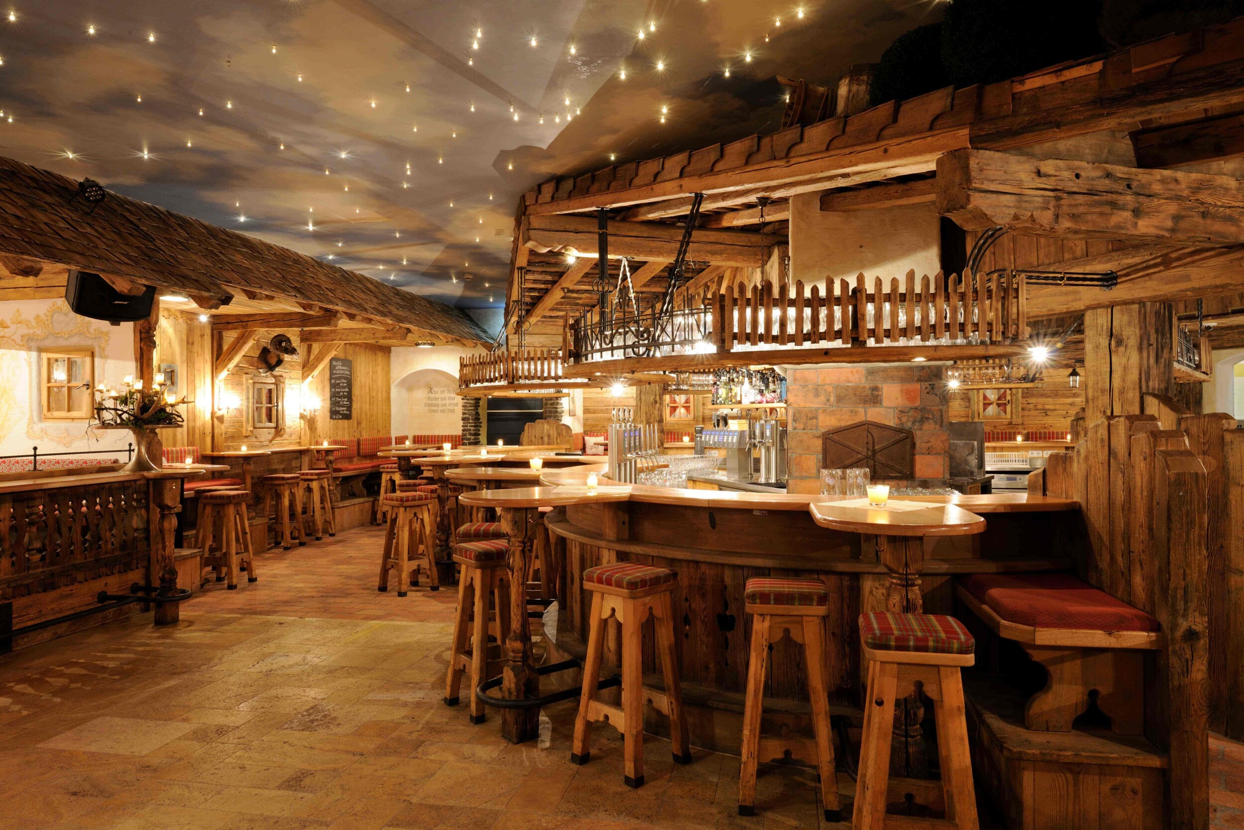 Ein gemütliches Gasthaus mit einem rustikalen Interieur, Holztischen und Stühlen, Schatten an den Wänden und einer Decke, die mit kleinen Lichterketten dekoriert ist.